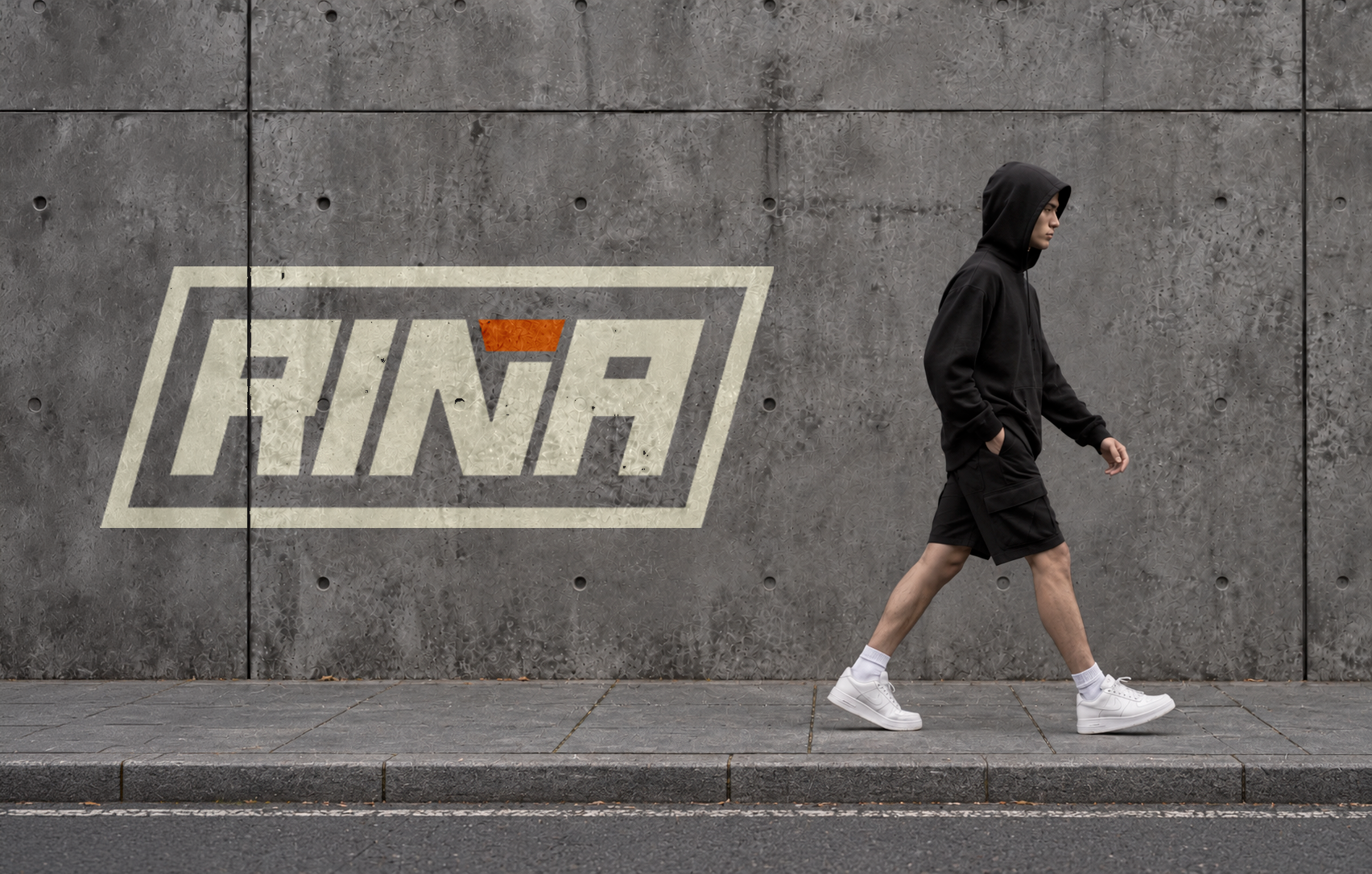 Persona vistiendo indumentaria negra frente a una pared con el logotipo de RIÑA